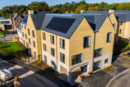 Front exterior view of York Manor Care Home, a welcoming brick building surrounded by well-maintained greenery and colorful flower beds, with clear signage at the entrance and large windows letting in natural light.