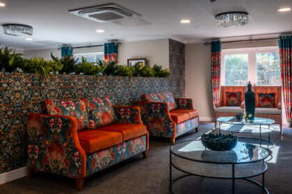 Bright and inviting sitting area in York Manor Care Home, featuring cozy armchairs in a variety of cheerful colors, soft cushions, and a coffee table with fresh flowers. Large windows fill the space with natural light, creating a warm and welcoming atmosphere.