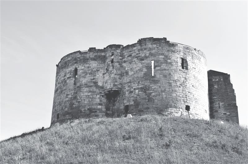 Clifford's Tower in York, a historic circular stone structure made of creamy limestone, perched atop a grassy motte. The tower, part of the medieval York Castle, offers panoramic views of the city and has a rich history dating back to the 11th century, including its role in the tragic 1190 massacre of York’s Jewish community